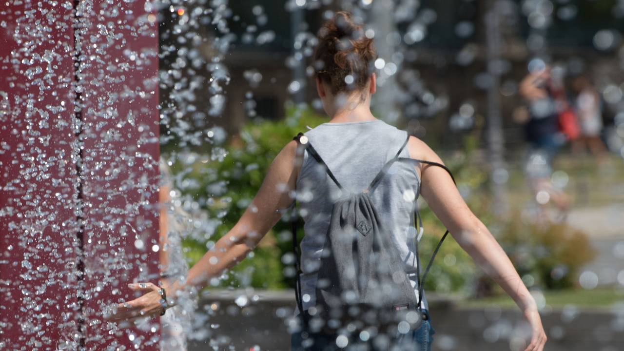 Eine Frau kühlt sich an einem Springbrunnen ab.