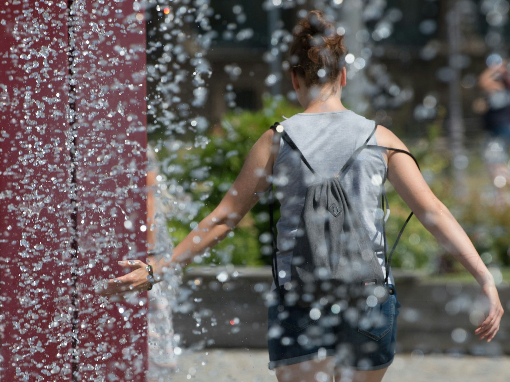 Eine Frau kühlt sich an einem Springbrunnen ab.