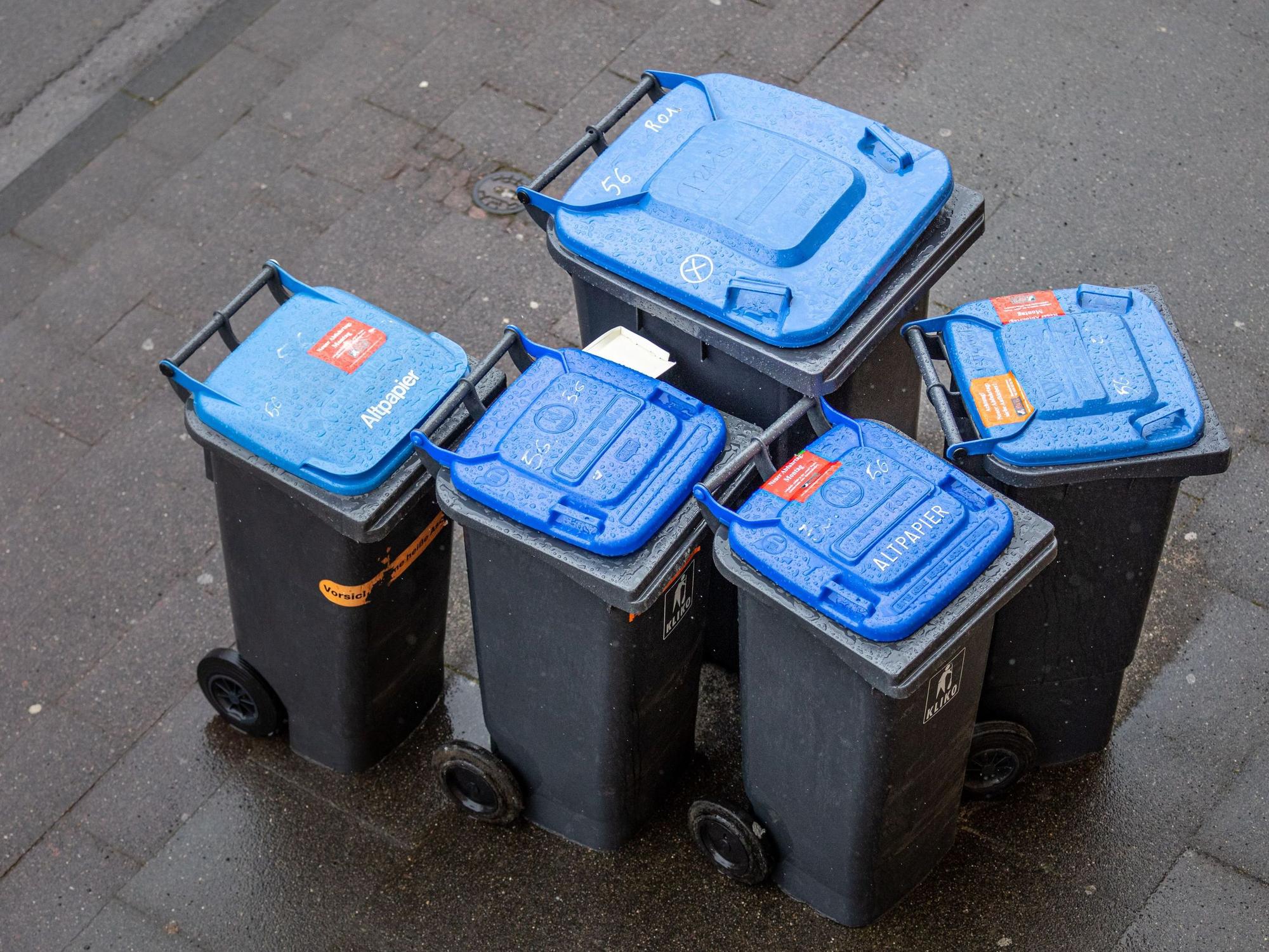 Abfalltonnen mit blauem Deckel, umgangssprachlich auch „Blaue Tonne“ genannt, für Altpapier stehen zur Abholung der AWB (Kölner Abfallwirtschaftsbetriebe) am Straßenrand.