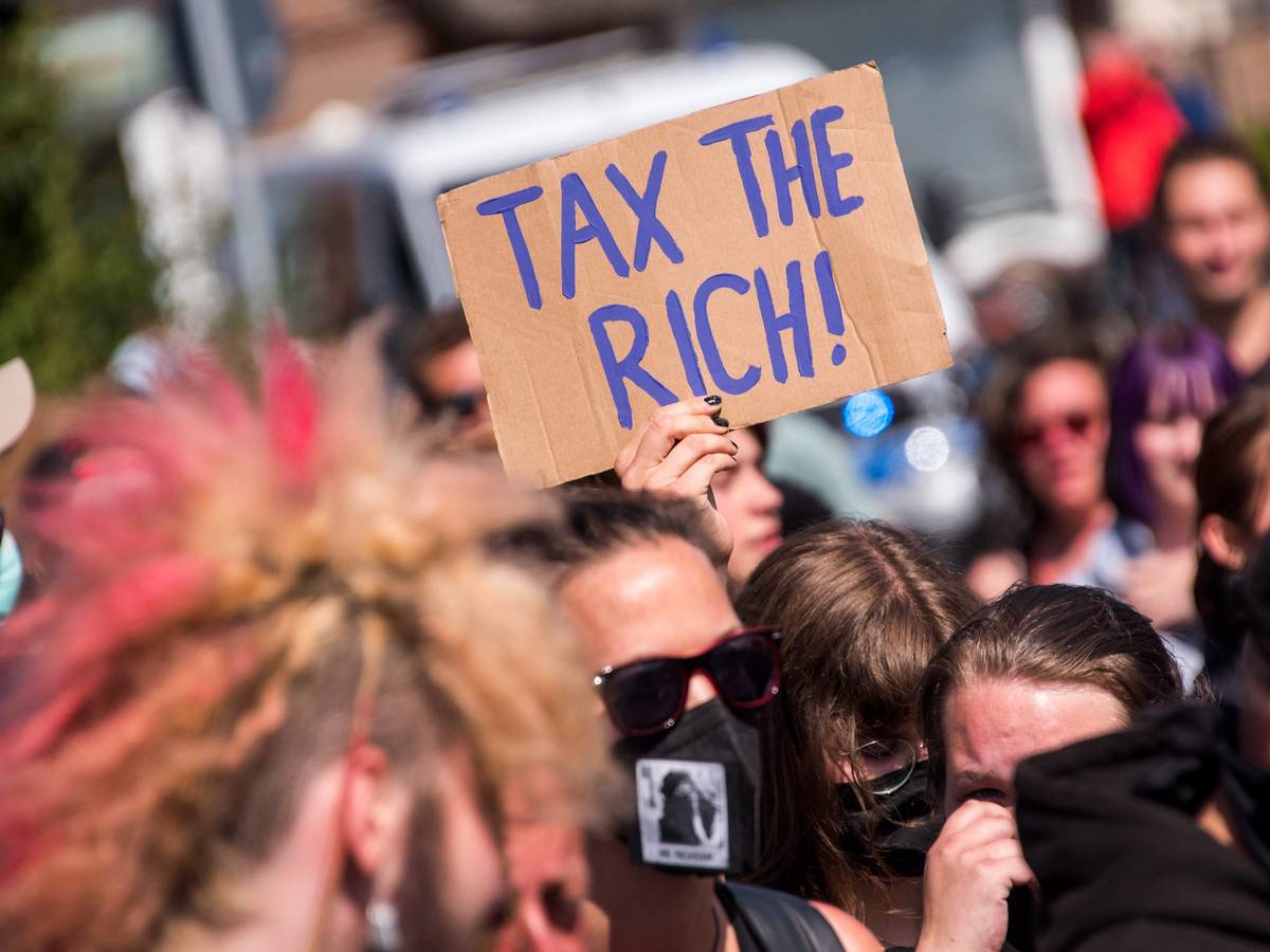 Teilnehmer einer Demonstrantion des Bündnisses „Wer hat, der gibt“ halten ein Schild mit der Aufschrift „Tax The Rich!“.