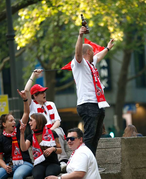 Fußballfans, die Schals des 1. FC Köln tragen, feiern.