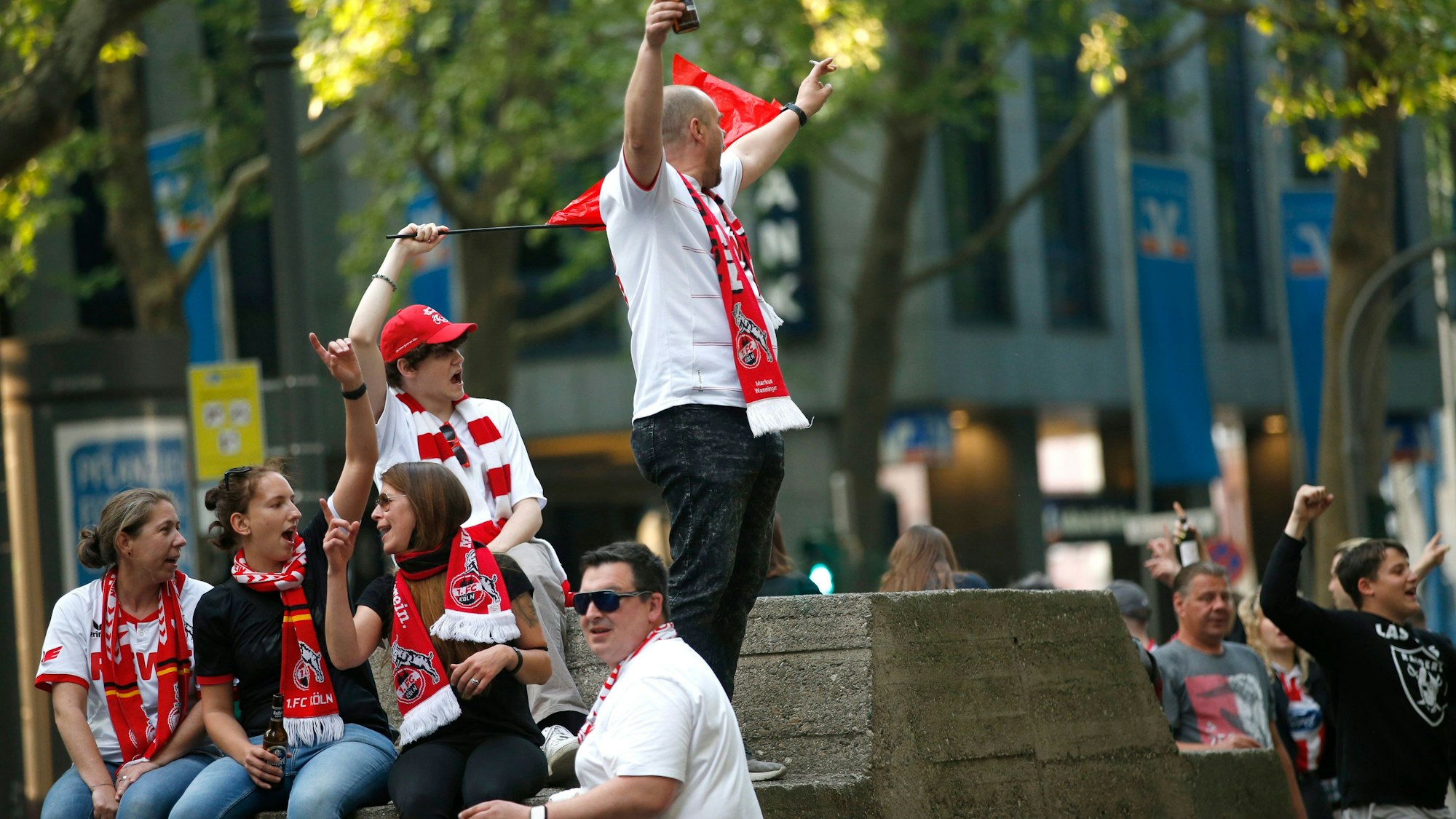 Fußballfans, die Schals des 1. FC Köln tragen, feiern.