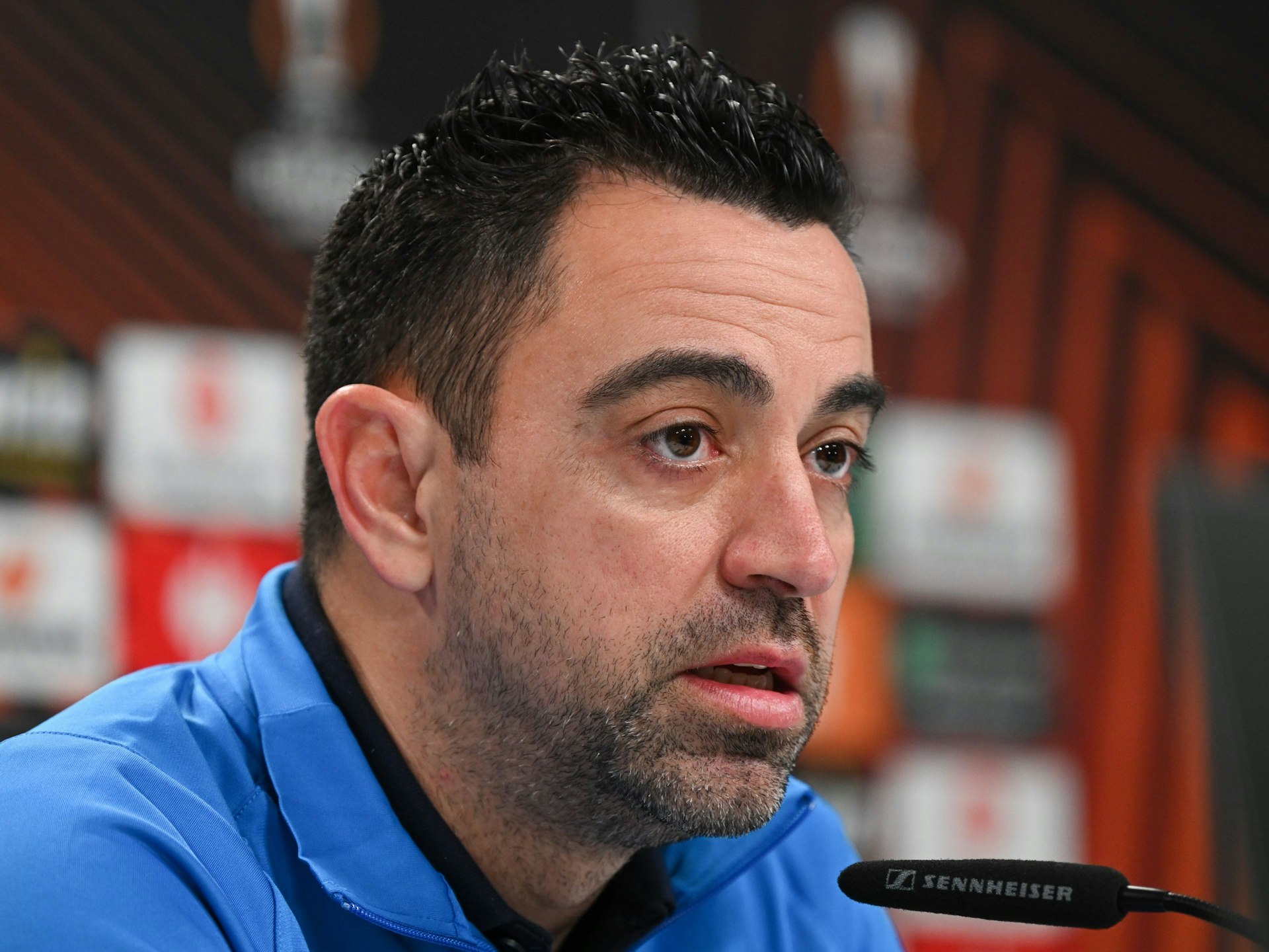 Cheftrainer Xavi Hernandez spricht bei einer Pressekonferenz in ein Mikrofon.