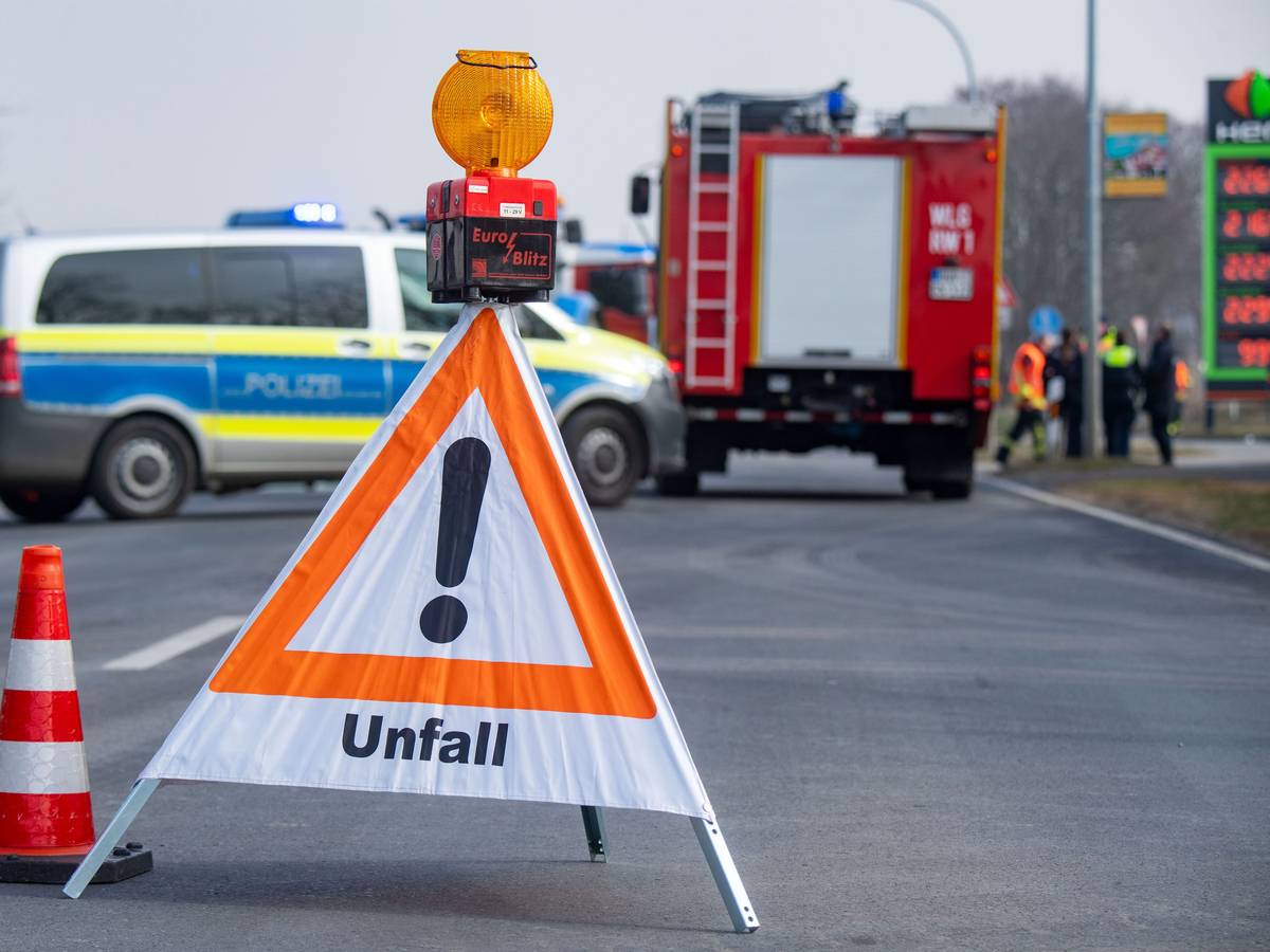 Ein Schild mit dem Hinweis „Unfall“ steht auf der Straße und hinten stehen Polizei- und Feuerwehrfahrzeuge.