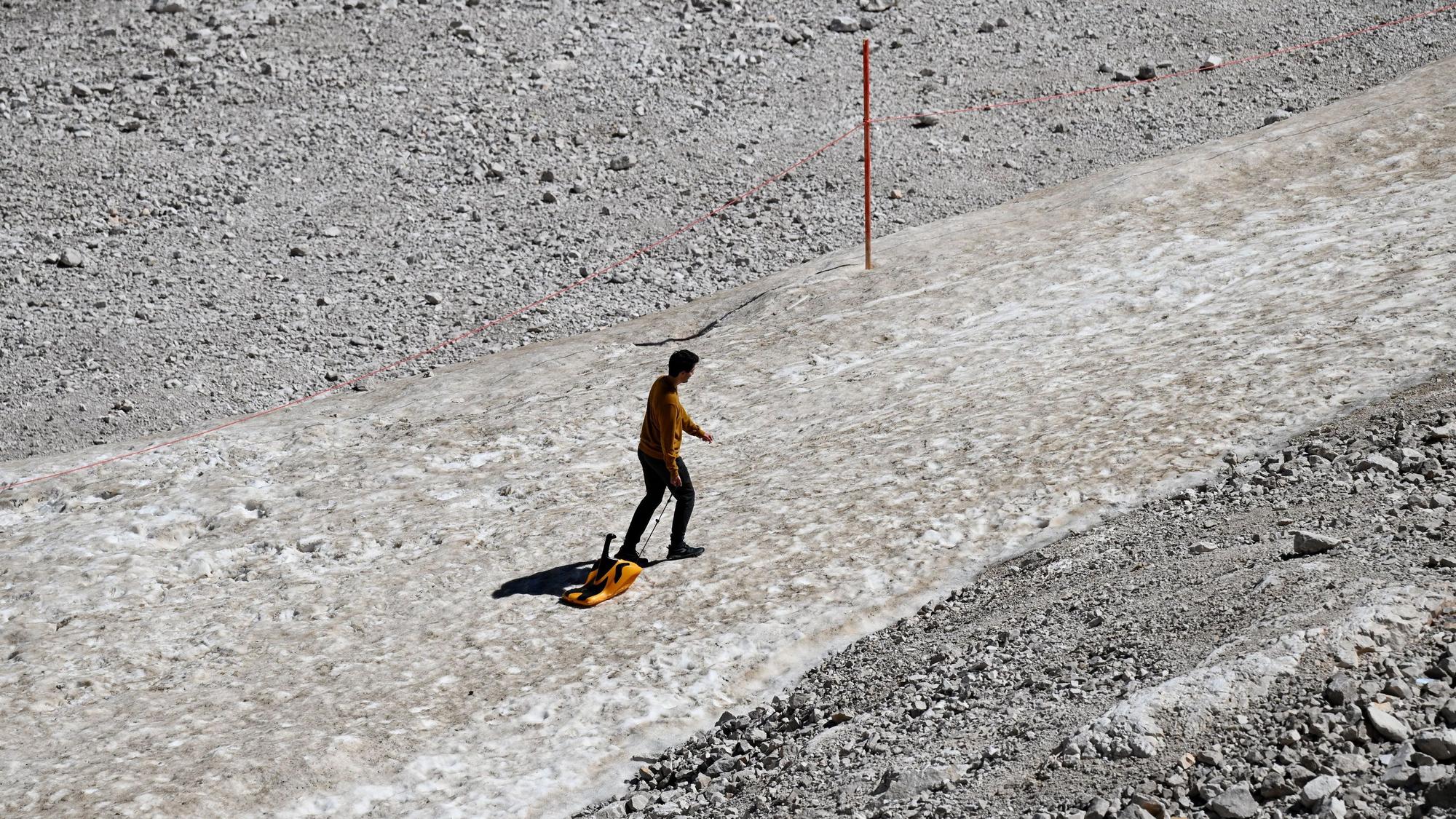 Ein Urlauber zieht auf dem Zugspitzplatt einen Schlitten über einen Schneerest.
