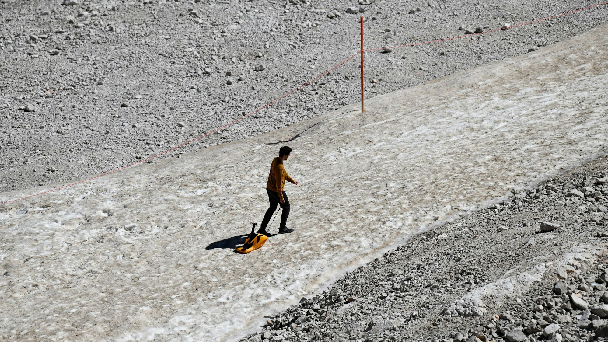 Ein Urlauber zieht auf dem Zugspitzplatt einen Schlitten über einen Schneerest.