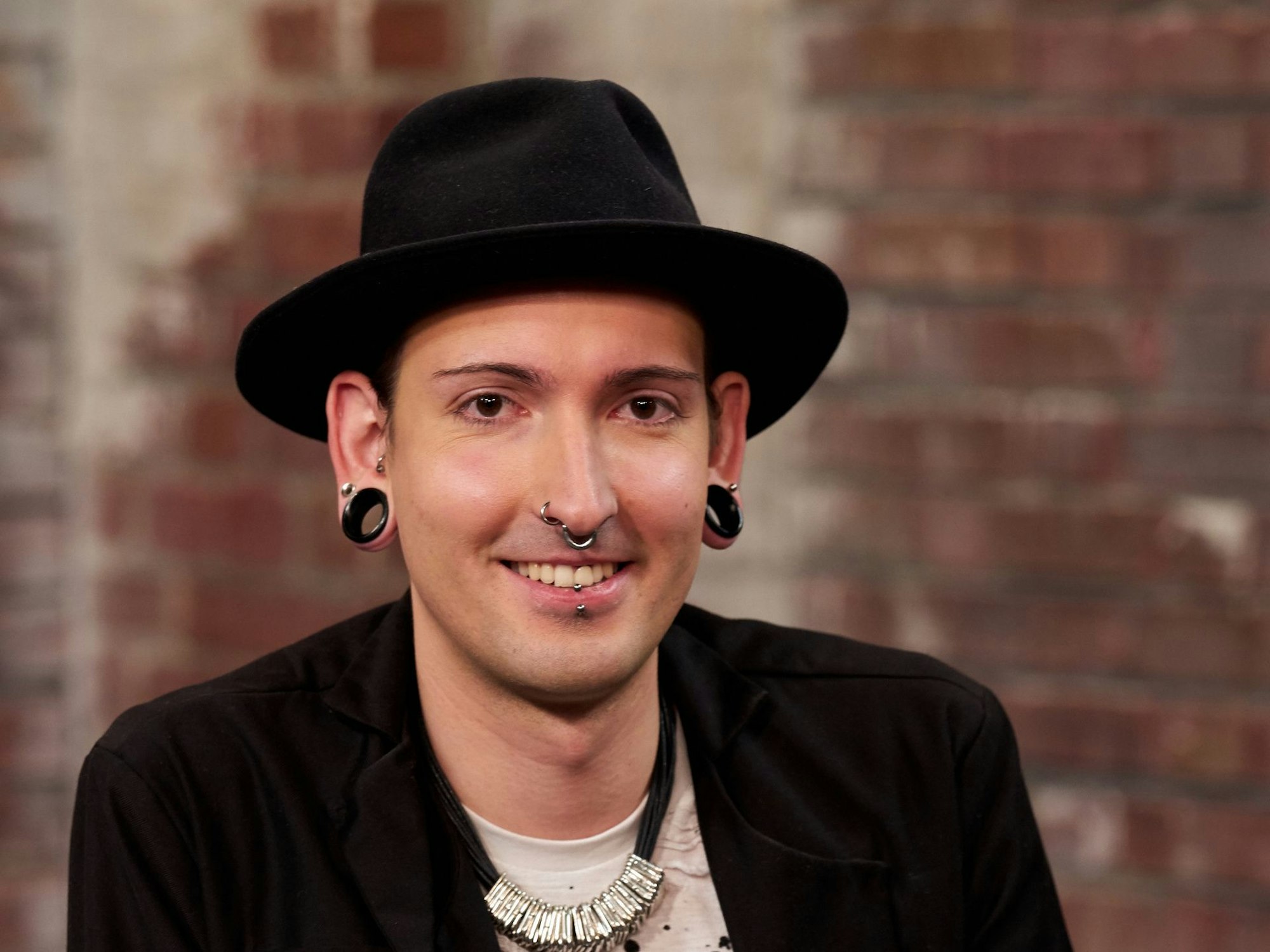 Das Foto zeigt Fabian Kahl bei einem Fototermin zur ZDF-Show „Bares für Rares“. Der Händler sitzt in der Studiokulisse und grinst.