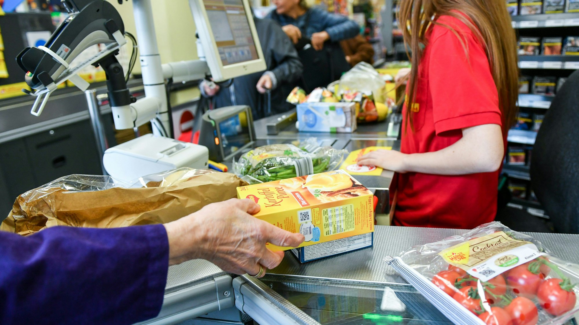Eine Kundin nimmt in einem Supermarkt Waren vom Band an der Kasse, nachdem eine Kassiererin die Waren gescannt hat.