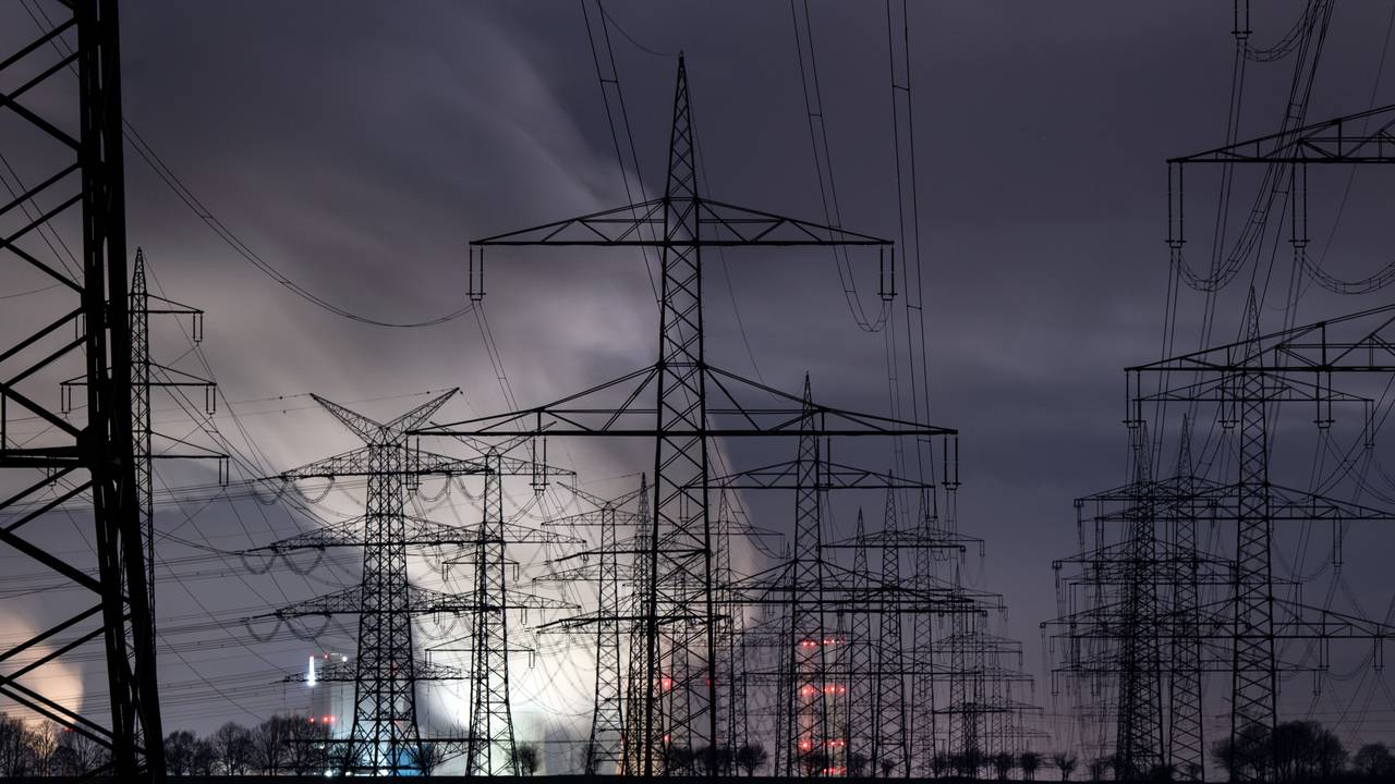 Hinter zahlreichen Strommasten zeichnet sich heller Dampf über dem Braunkohlekraftwerk Niederaußem vor dem noch dunklen Morgenhimmel ab.