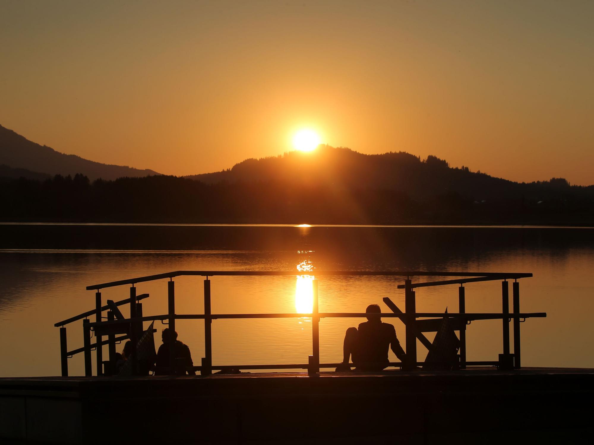 Menschen genießen am Ufer des Hopfensees den Sonnenuntergang.