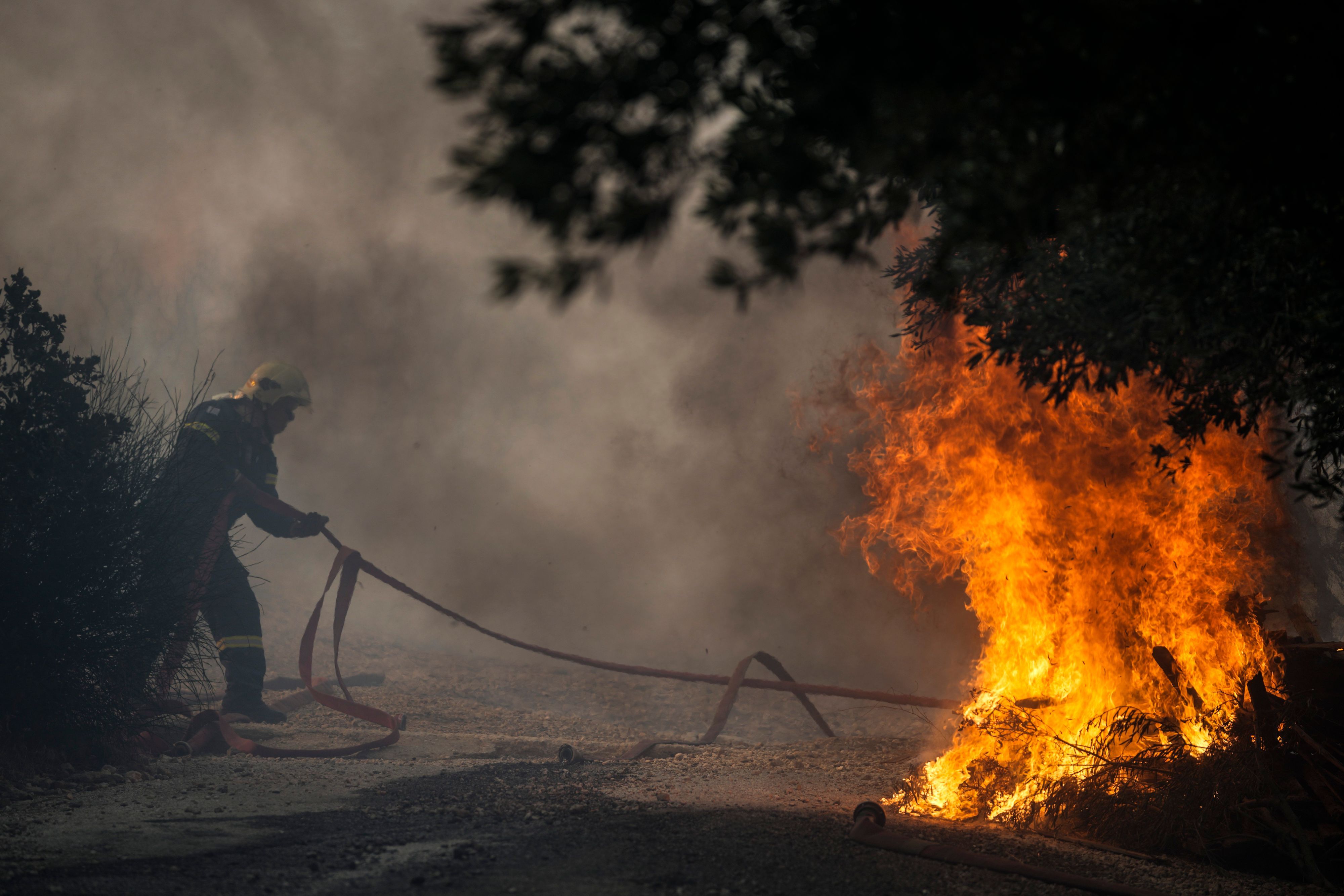 Ein Feuerwehrmann zieht einen Schlauch, während das Feuer in der Nähe eines Hauses am Berg Penteli, nordöstlich von Athen, Dienstag, 19. Juli 2022, brennt.