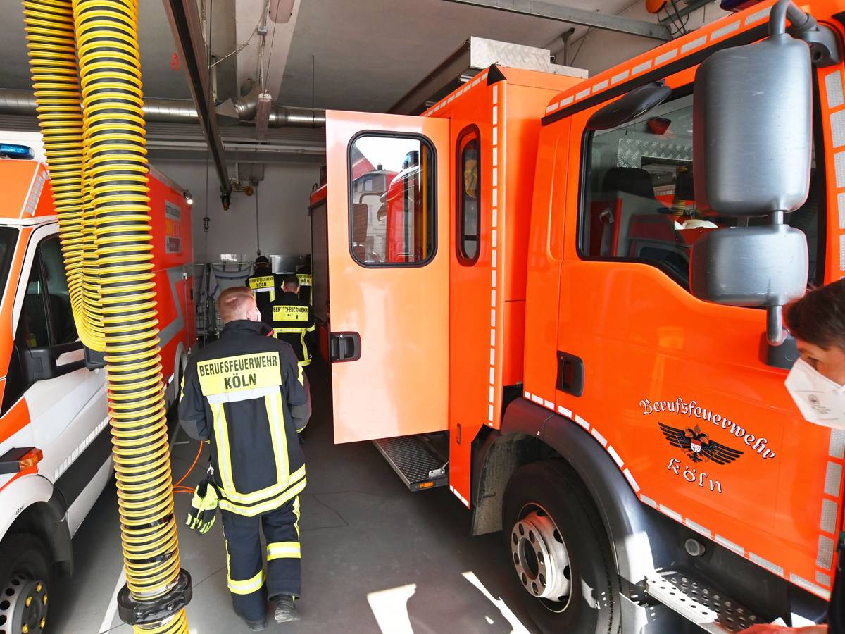 Einsatzkräfte der Feuerwehr Köln laufen an Einsatzfahrzeugen vorbei.
