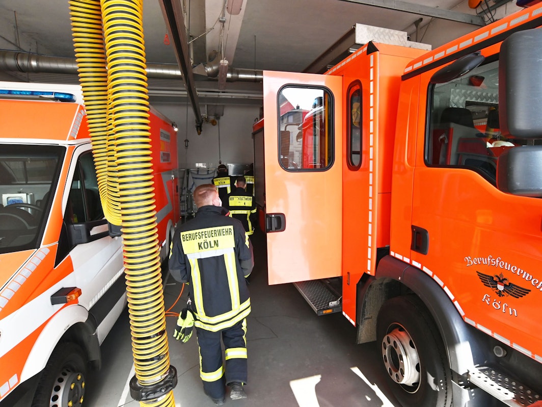 Einsatzkräfte der Feuerwehr Köln laufen an Einsatzfahrzeugen vorbei.