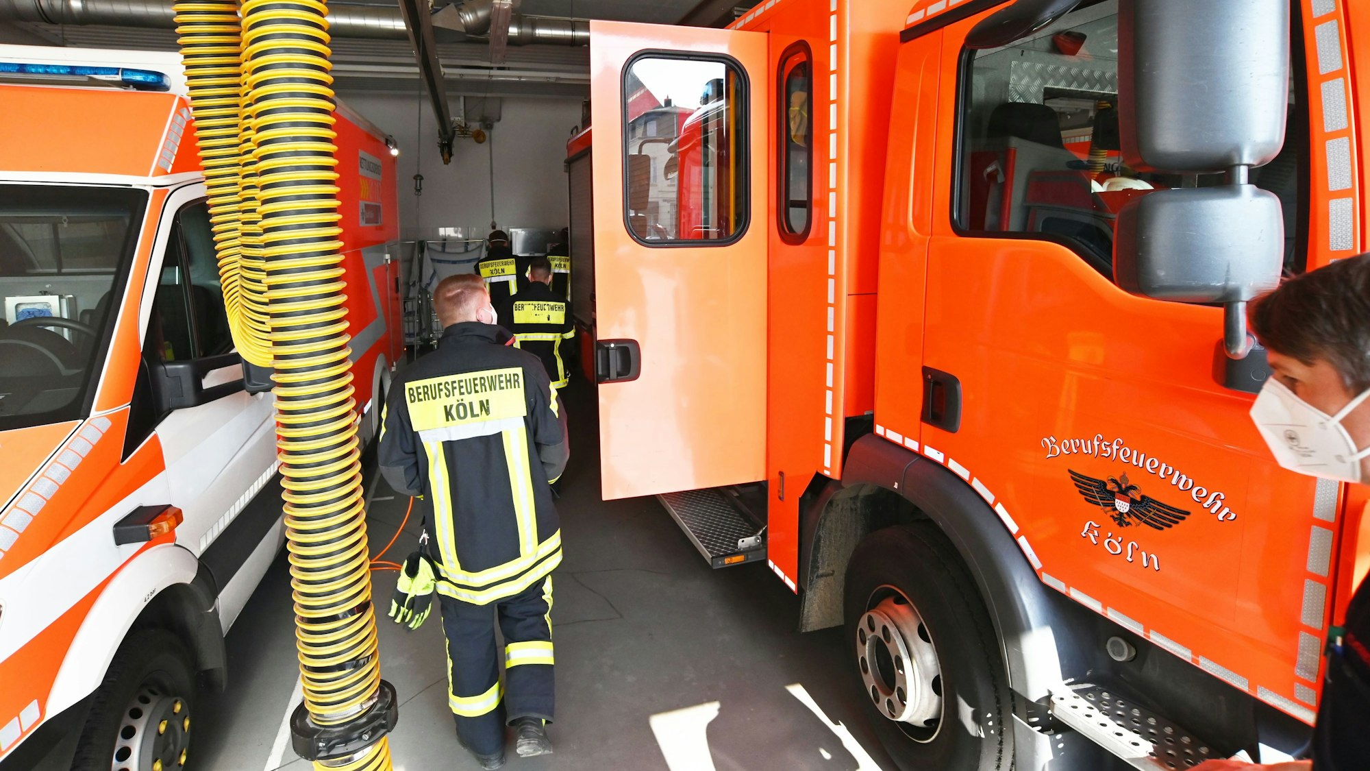 Kräfte der Kölner Berufsfeuerwehr gehen zwischen einem Löschfahrzeug und einem Rettungswagen entlang.