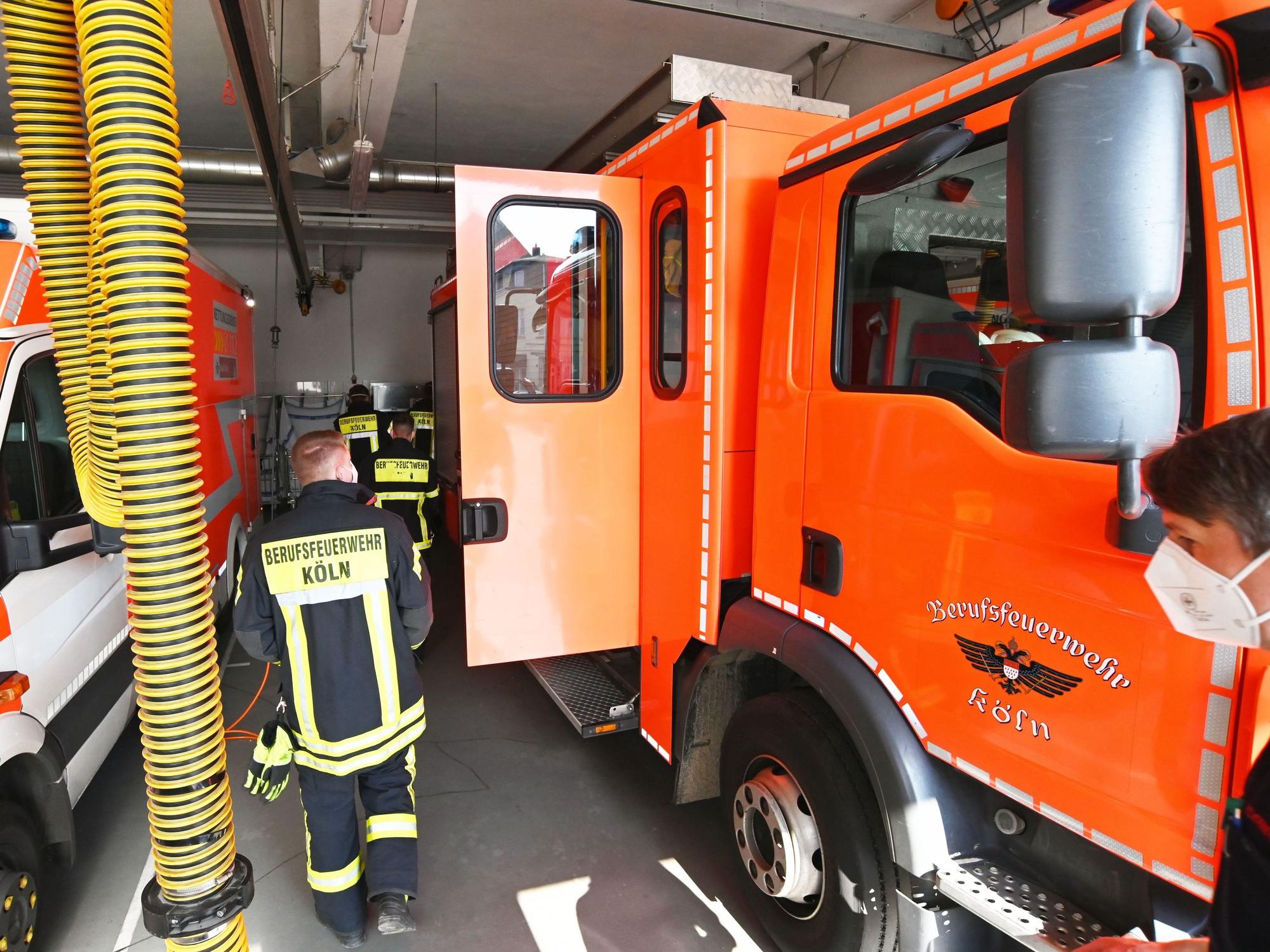 Einsatzkräfte der Feuerwehr Köln laufen an Einsatzfahrzeugen vorbei.