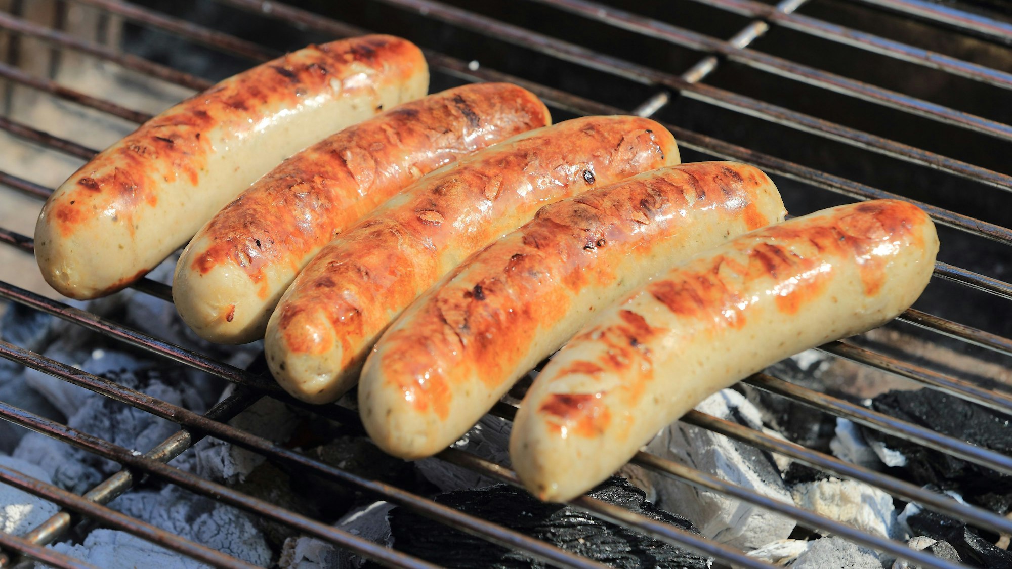 Bratwürste liegen auf einem Holzkohle-Grill.