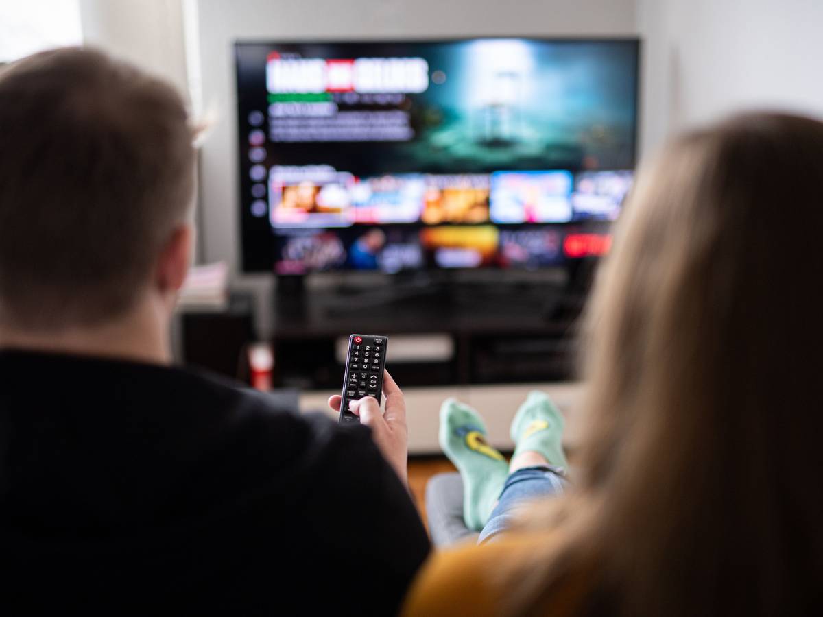 Zuschauer sitzen vor einem Fernseher und schauen sich das Streaming-Angebot ihrer Abonnements an.
