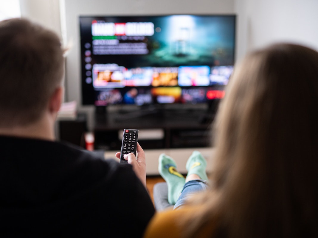 Zuschauer sitzen vor einem Fernseher und schauen sich das Streaming-Angebot ihrer Abonnements an.
