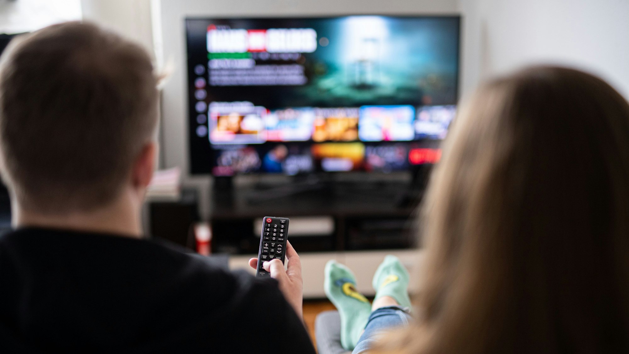 Zuschauer sitzen vor einem Fernseher und schauen sich das Streaming-Angebot ihrer Abonnements an.
