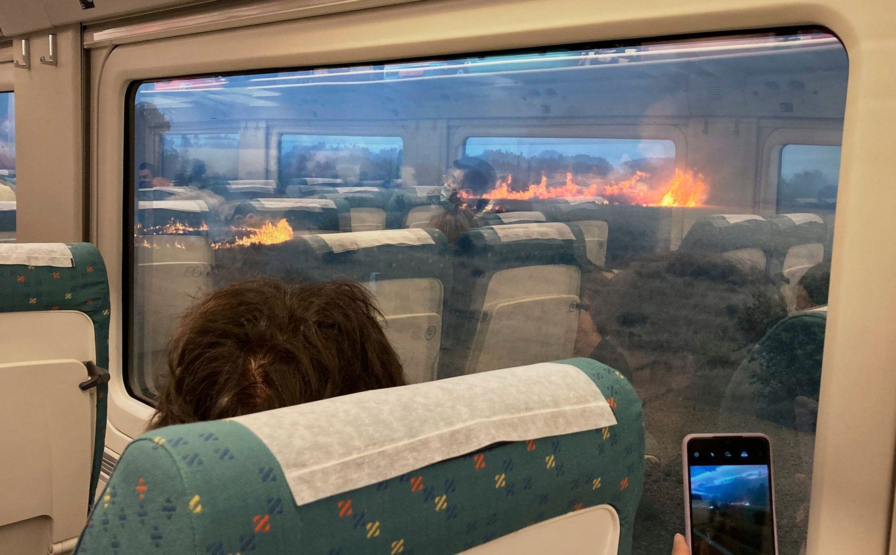 Fahrgäste fotografieren während einer Zugfahrt in Spanien einen Flächenbrand. Der Zug hielt unterwartet in einer Region an, in der sich die Flammen ausbreiteten.