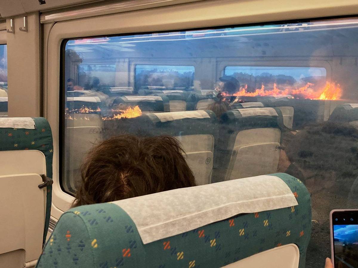 Fahrgäste fotografieren während einer Zugfahrt in Spanien einen Flächenbrand. Der Zug hielt unterwartet in einer Region an, in der sich die Flammen ausbreiteten.
