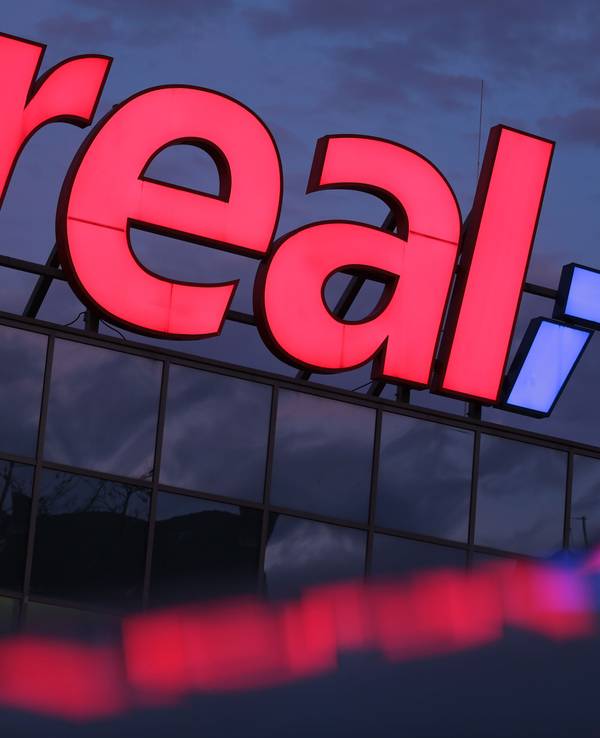 Das Logo leuchtet am Morgen auf dem Dach eines Real Supermarktes.