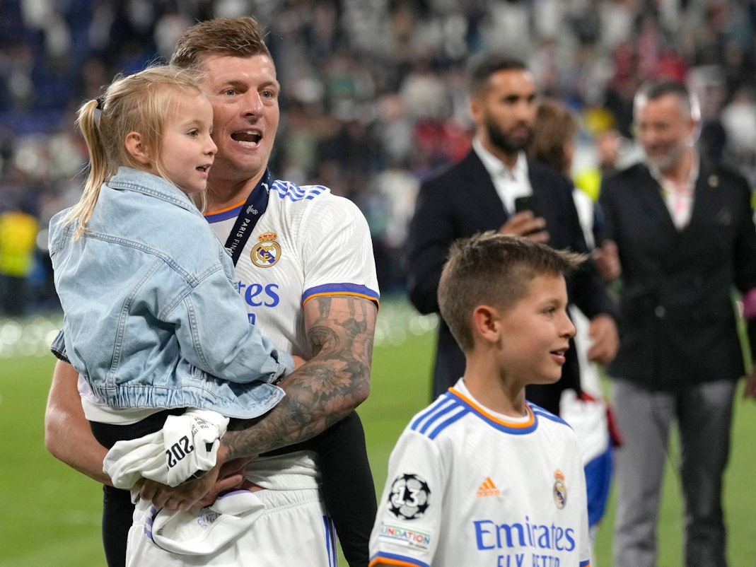 Toni Kroos steht auf dem Platz und hält seine Tochter auf dem Arm, daneben sein Sohn.