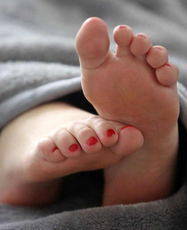 Eine Frau schläft in einem Bett und streckt die Füße unter der Decke hervor.