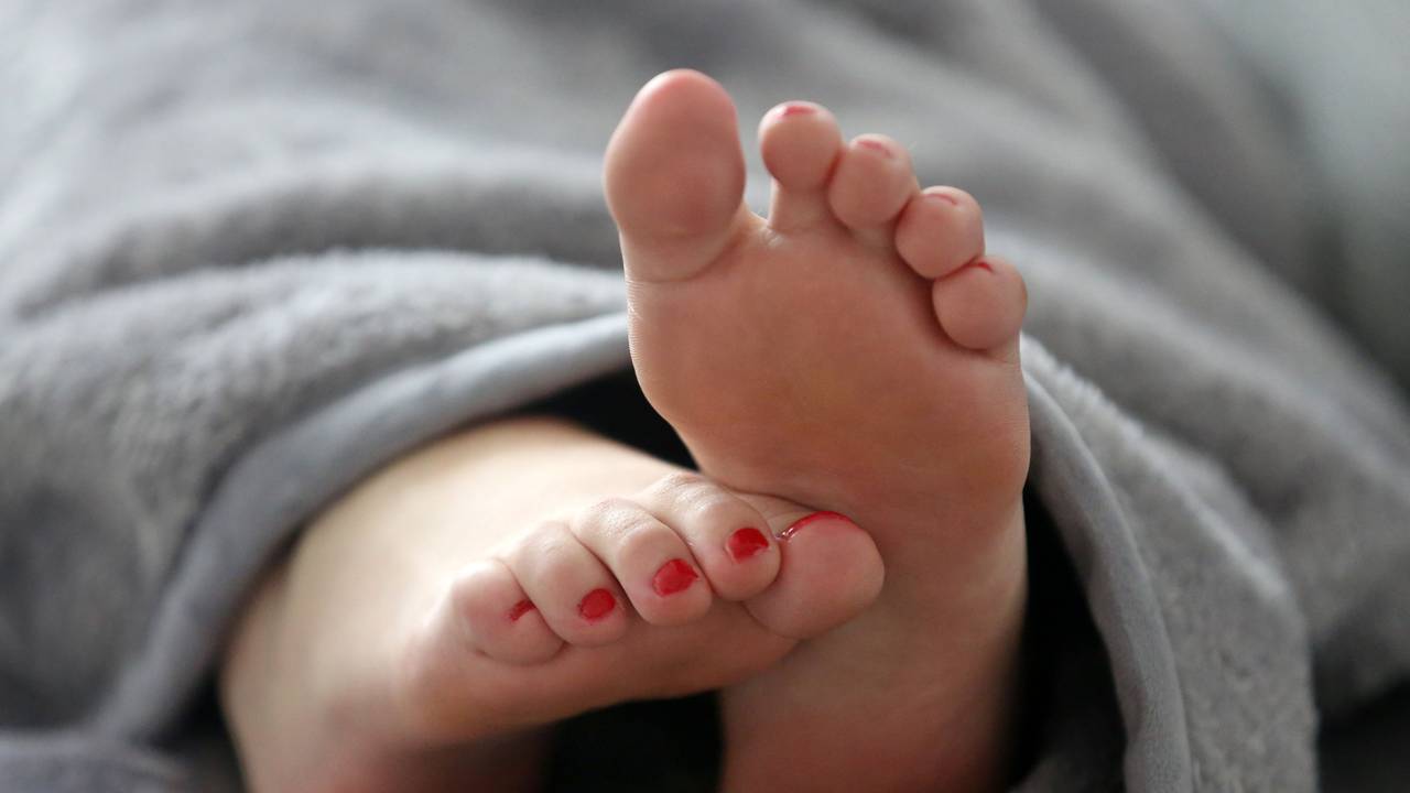 Eine Frau schläft in einem Bett und streckt die Füße unter der Decke hervor.