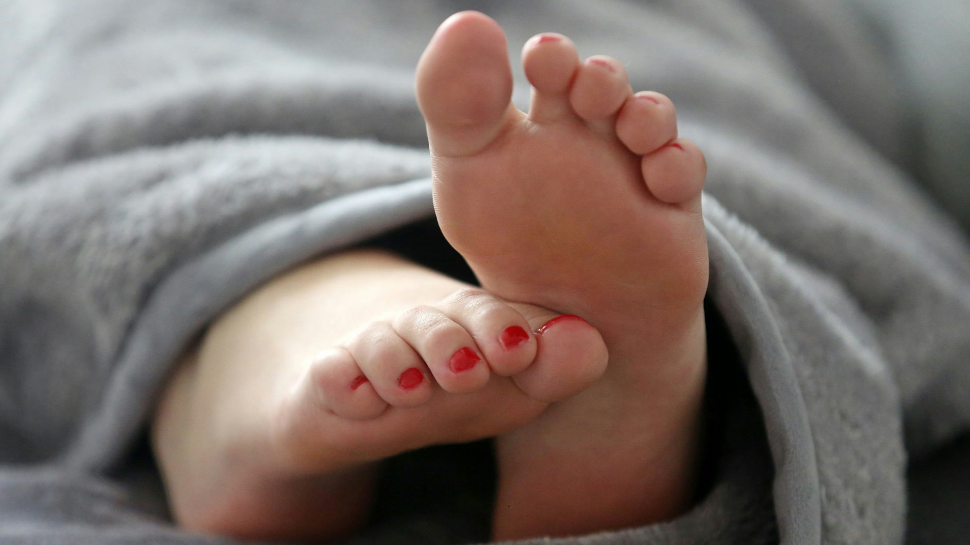 Eine Frau schläft in einem Bett und streckt die Füße unter der Decke hervor.
