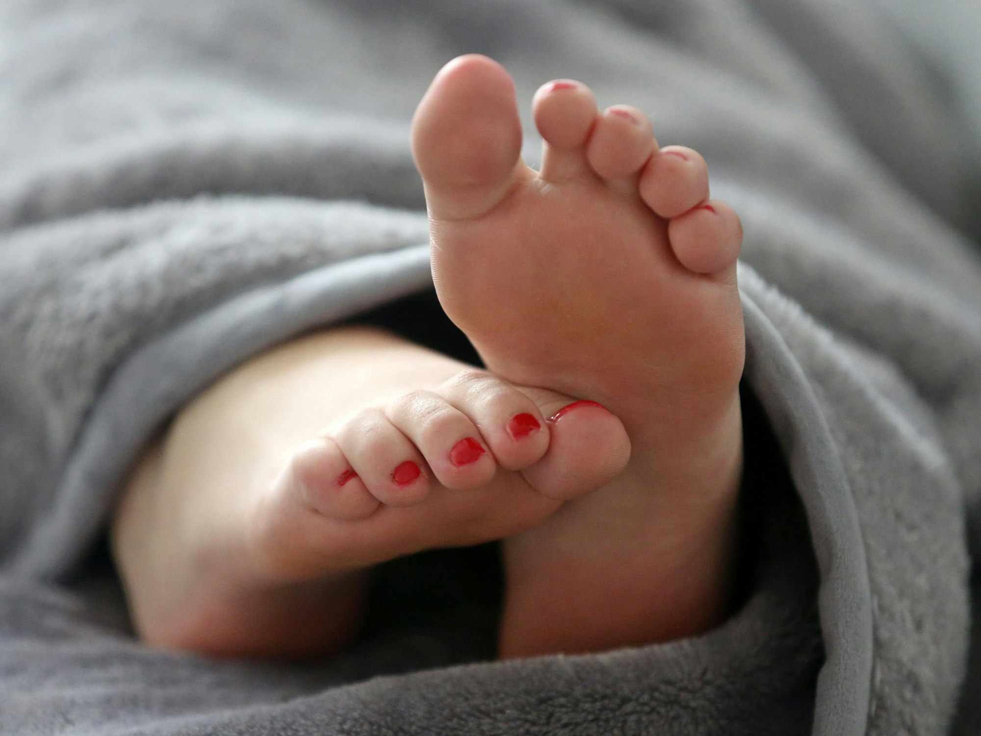 Eine Frau schläft in einem Bett und streckt die Füße unter der Decke hervor.