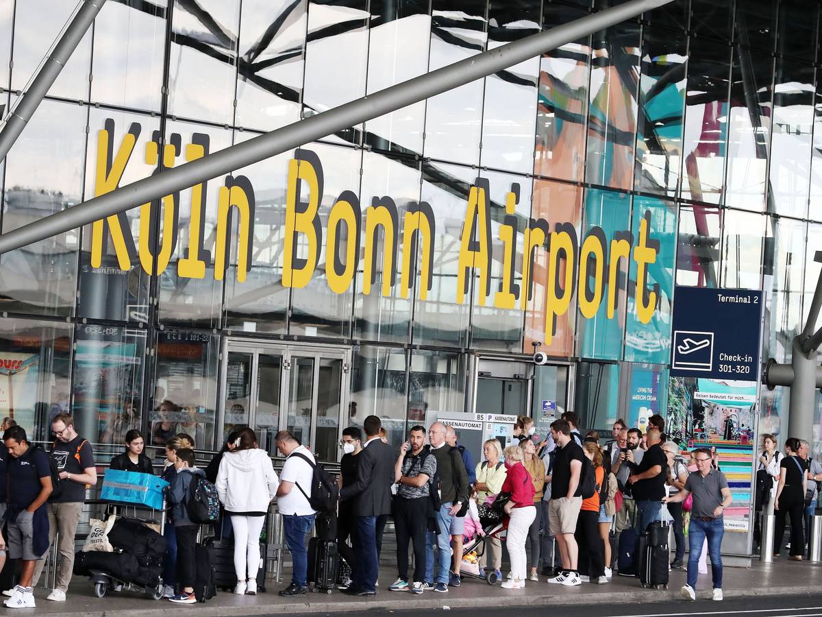 Fluggäste stehen am Flughafen Köln/Bonn in der Warteschlange, die bis vor das Terminal reicht.