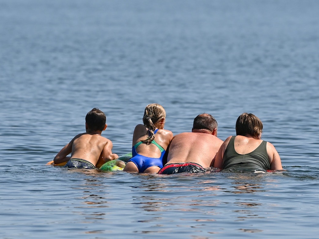 Eine Familie schwimmt auf einer Luftmatratze im Wasser des Storkower Sees.