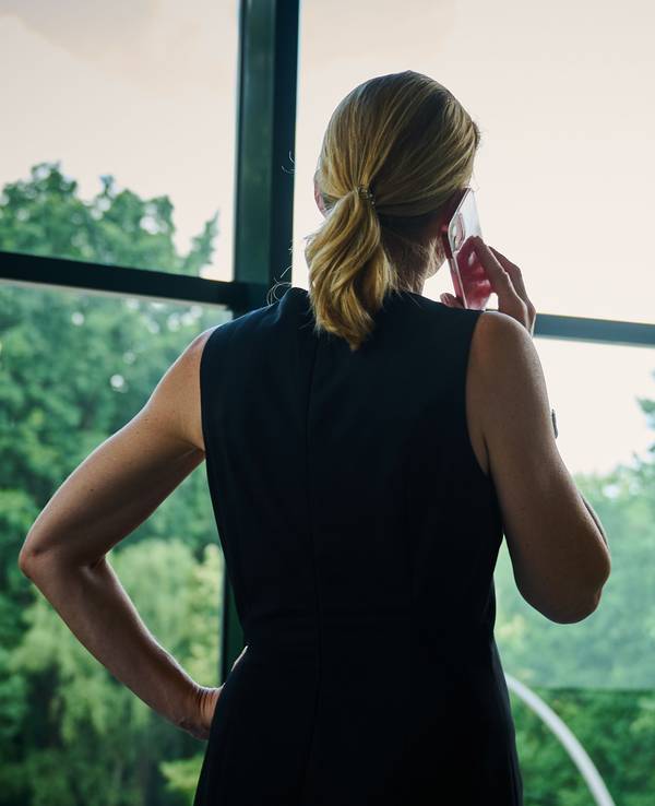 Eine Frau steht in einem Bürozimmer am Fenster und telefoniert.
