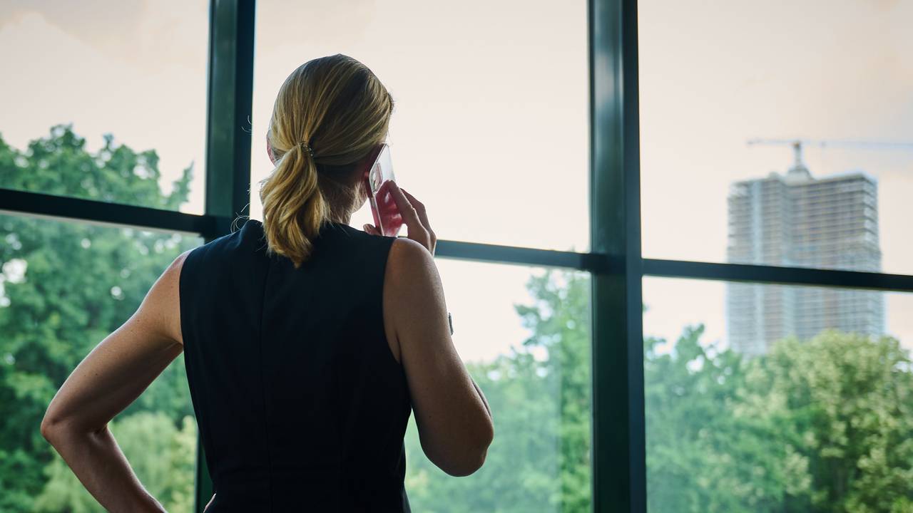 Eine Frau steht in einem Bürozimmer am Fenster und telefoniert.