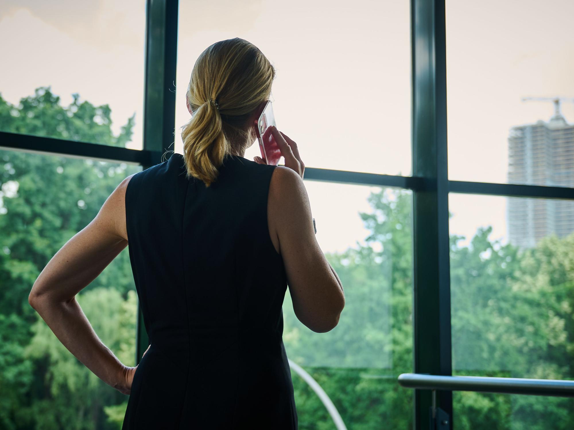 Eine Frau steht in einem Bürozimmer am Fenster und telefoniert.