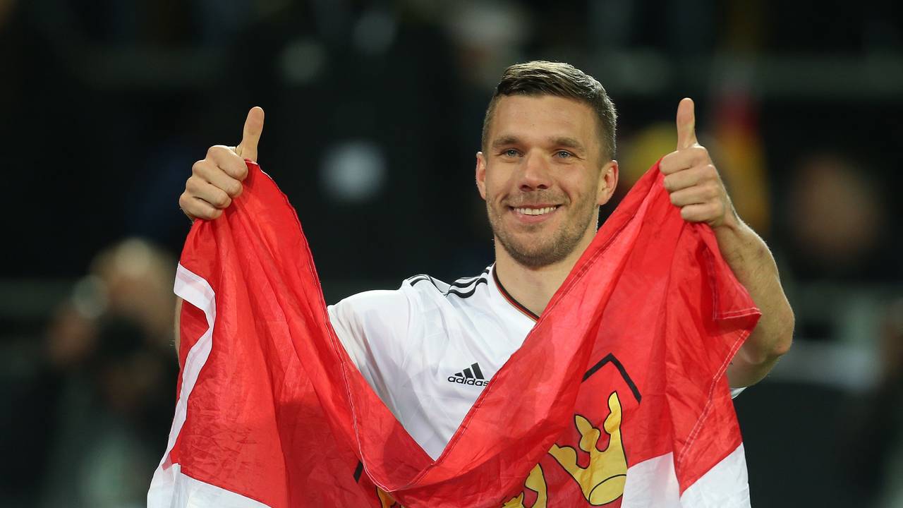 Lukas Podolski aus Deutschland verabschiedet sich nach dem Spiel von den Fans und hält dabei eine Kölner Fahne.