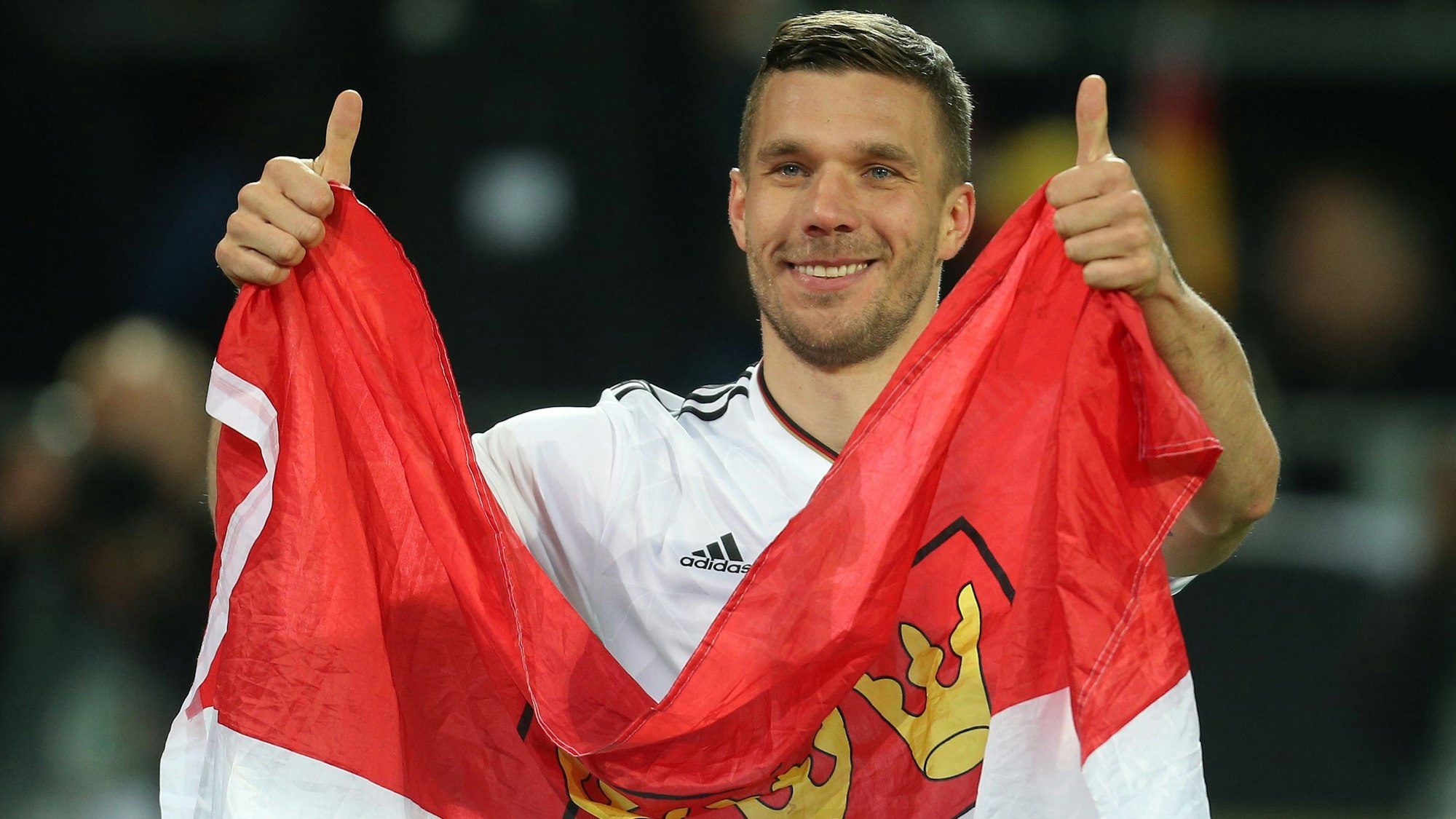Lukas Podolski aus Deutschland verabschiedet sich nach dem Spiel von den Fans und hält dabei eine Kölner Fahne.