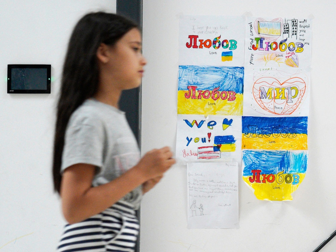 Ein junges Mädchen, das aus der Ukraine geflohen ist, läuft Mitte Juli in Warschau an mehreren Kinderzeichnungen vorbei, auf denen „Frieden“ und „Liebe“ steht. Viele Familien sind gefangen zwischen dem Wunsch, zurückzukehren und der Angst vor der Notwendigkeit, sich etwas Neues aufzubauen.