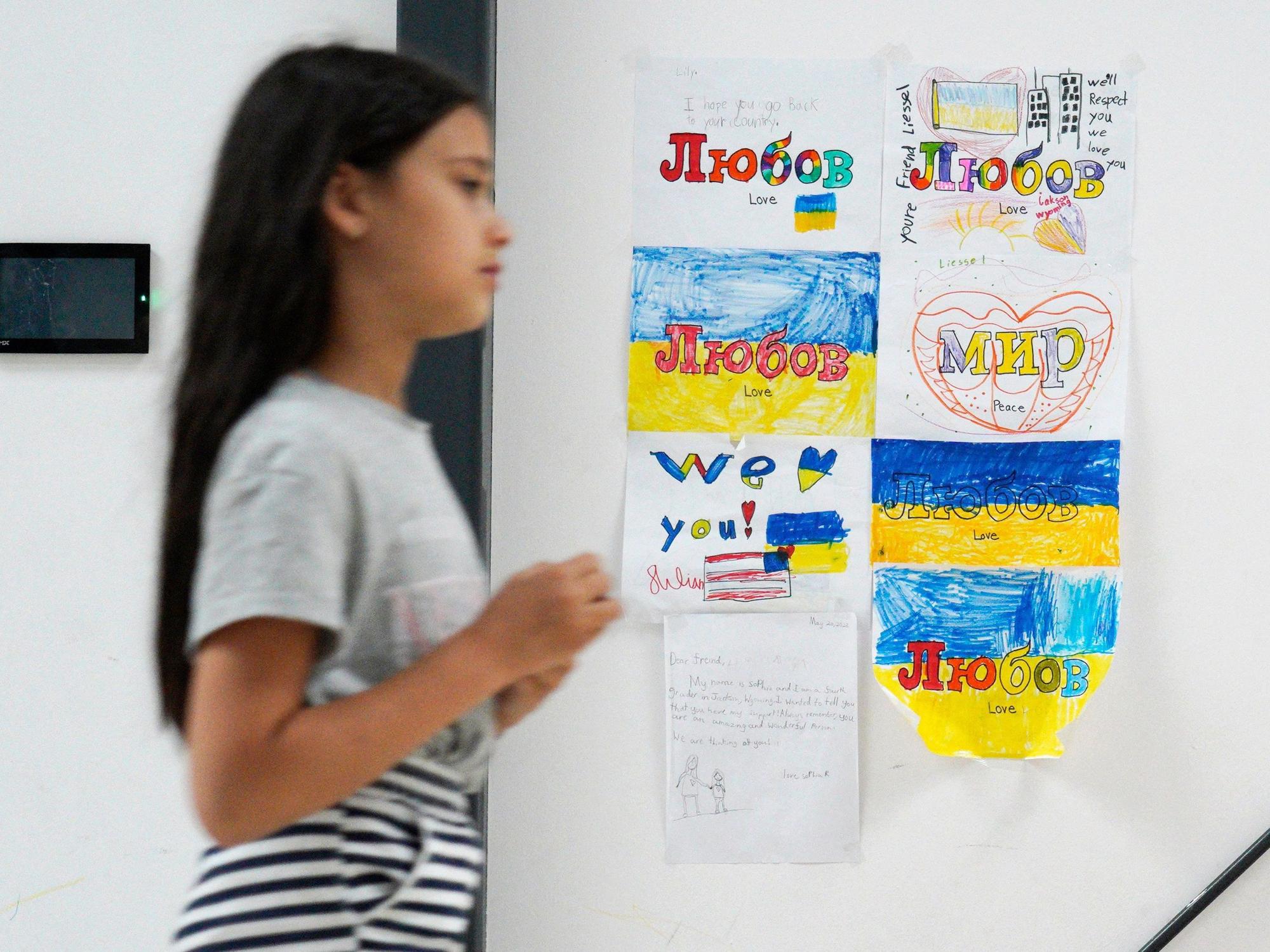 Ein junges Mädchen, das aus der Ukraine geflohen ist, läuft Mitte Juli in Warschau an mehreren Kinderzeichnungen vorbei, auf denen „Frieden“ und „Liebe“ steht. Viele Familien sind gefangen zwischen dem Wunsch, zurückzukehren und der Angst vor der Notwendigkeit, sich etwas Neues aufzubauen.