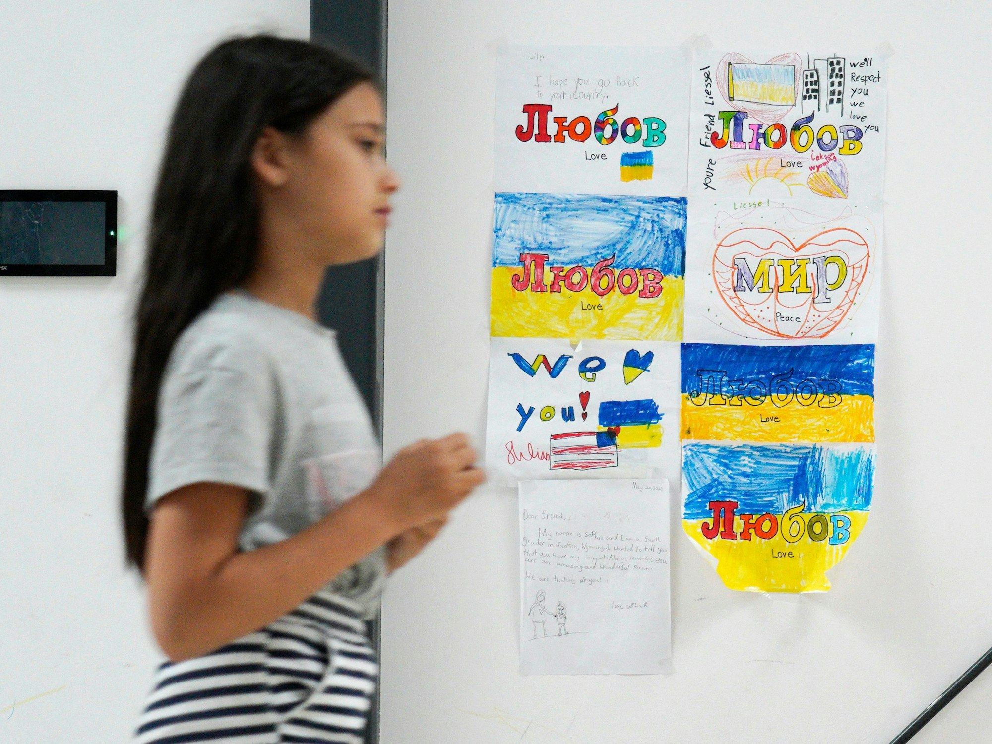 Ein junges Mädchen, das aus der Ukraine geflohen ist, läuft Mitte Juli in Warschau an mehreren Kinderzeichnungen vorbei, auf denen „Frieden“ und „Liebe“ steht. Viele Familien sind gefangen zwischen dem Wunsch, zurückzukehren und der Angst vor der Notwendigkeit, sich etwas Neues aufzubauen.