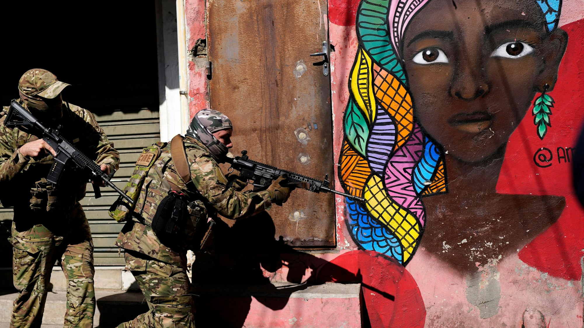 Bei einem Polizeieinsatz am 21. Juli 2022 in Rio de Janeiro sind 18 Menschen gestorben. Hier sind zwei bewaffnete Polizisten an einer bemalten Häuserwand im Viertel „Complexo do Alemão“ zu sehen.