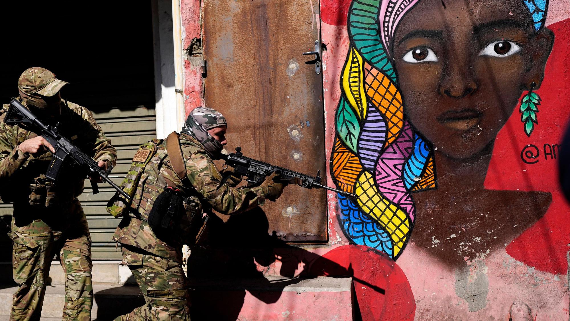 Bei einem Polizeieinsatz am 21. Juli 2022 in Rio de Janeiro sind 18 Menschen gestorben. Hier sind zwei bewaffnete Polizisten an einer bemalten Häuserwand im Viertel „Complexo do Alemão“ zu sehen.