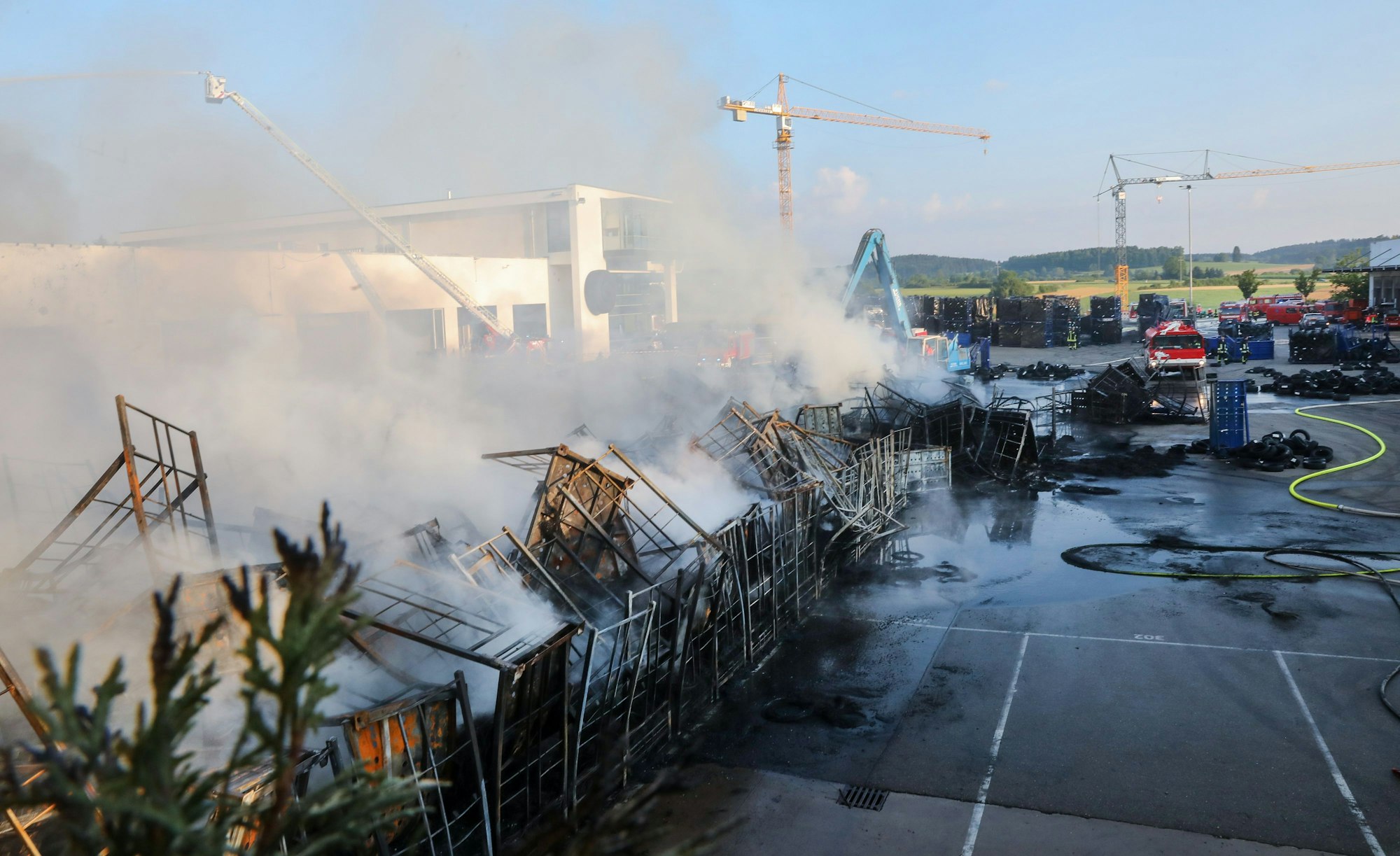 Einsatzkräfte der Feuerwehr stehen während eines Großbrandes auf dem Gelände eines Reifengroßhändlers und löschen das Feuer.