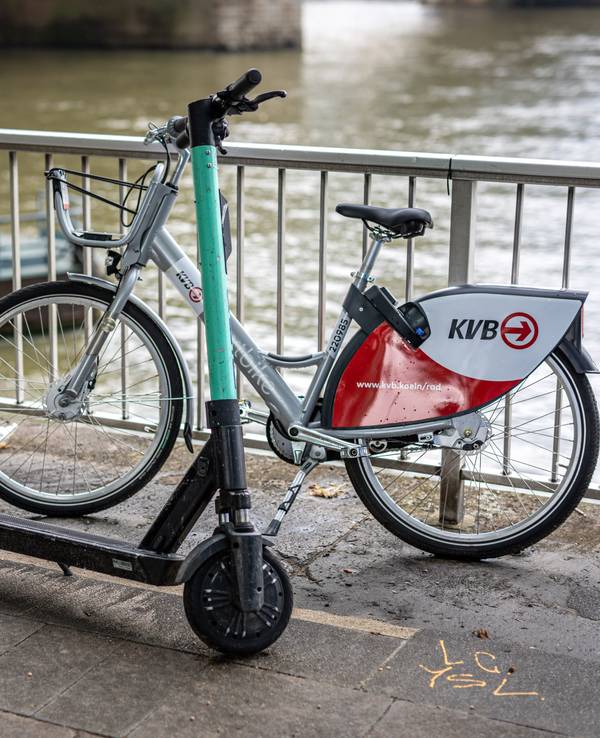 Ein E-Scooter und ein Leihfahrrad der Kölner Verkehrsbetriebe (KVB) stehen am Rheinufer vor der Hohenzollernbrücke an der Kölner Altstadt am Geländer. Die KVB arbeitet ab sofort mit dem Mobilitätsdienstleister Bolt zusammen.