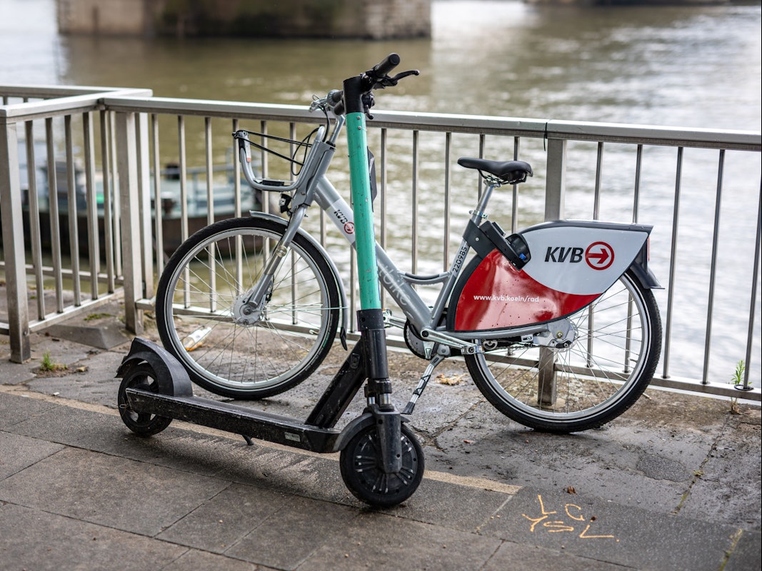 Ein E-Scooter und ein Leihfahrrad der Kölner Verkehrsbetriebe (KVB) stehen am Rheinufer vor der Hohenzollernbrücke an der Kölner Altstadt am Geländer. Die KVB arbeitet ab sofort mit dem Mobilitätsdienstleister Bolt zusammen.