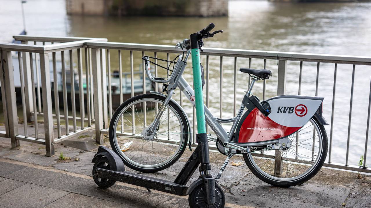 Ein E-Scooter und ein Leihfahrrad der Kölner Verkehrsbetriebe (KVB) stehen am Rheinufer vor der Hohenzollernbrücke an der Kölner Altstadt am Geländer. Die KVB arbeitet ab sofort mit dem Mobilitätsdienstleister Bolt zusammen.