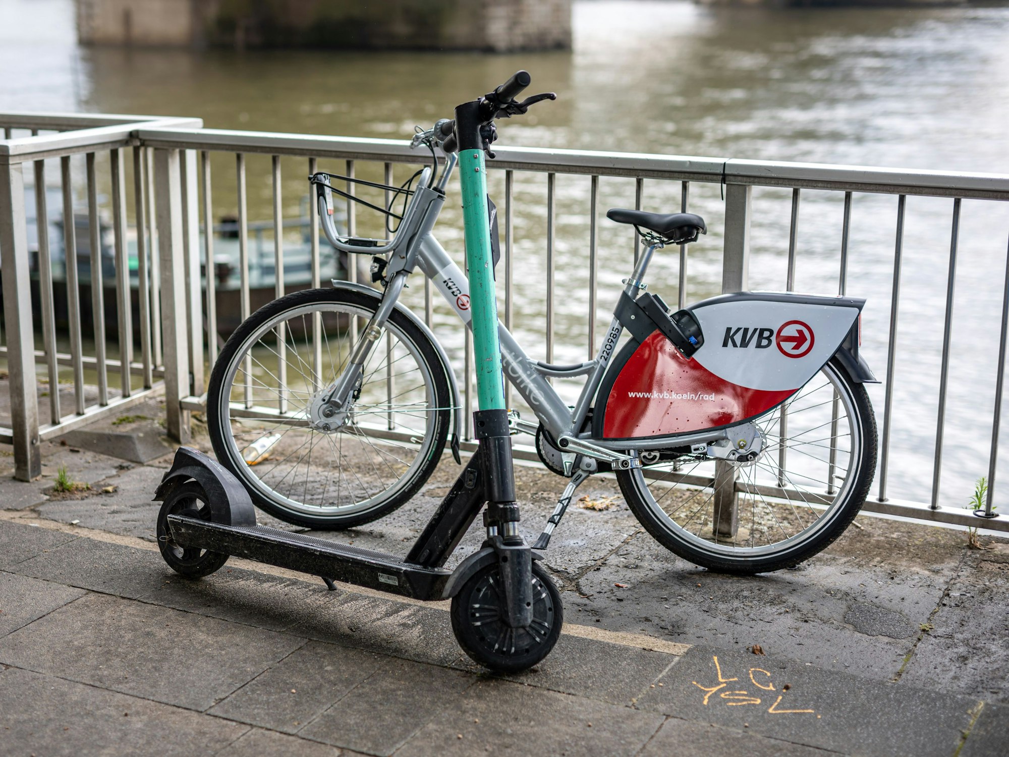 Ein E-Scooter und ein Leihfahrrad der Kölner Verkehrsbetriebe (KVB) stehen am Rheinufer vor der Hohenzollernbrücke an der Kölner Altstadt am Geländer. Die KVB arbeitet ab sofort mit dem Mobilitätsdienstleister Bolt zusammen.