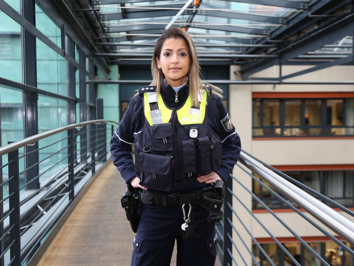 Polizistin Özlem Yagmur steht in einem Flur und lacht in die Kamera.