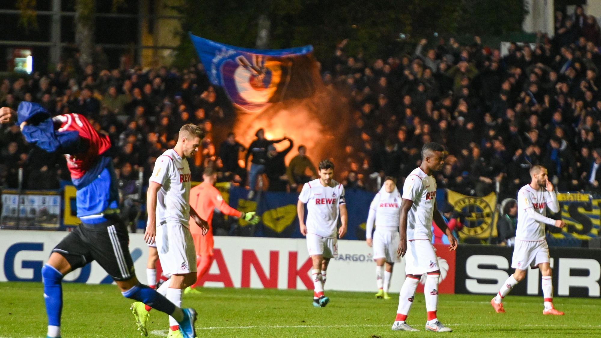 Die Spieler des 1. FC Köln lassen die Köpfe hängen, die Saarbrücken-Fans zünden Pyrotechnik.